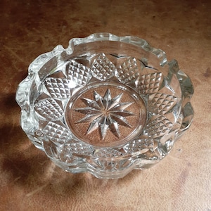 May include: A clear glass ashtray with a starburst design in the center and a diamond pattern around the edge.