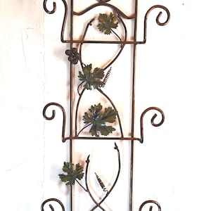 May include: A decorative metal wall hanging with a vine and leaf design. The brown metal frame features a rectangular shape with scrollwork and green-painted leaves. The wall decor is designed to be hung on a wall.
