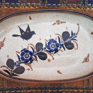 May include: Oval ceramic serving platter with a cream-colored base, featuring a dark blue bird and floral design. The flowers are blue with dark green leaves. The rim is brown with a dark blue border. Decorative and functional.