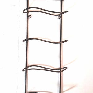 May include: A wrought iron wine rack with a decorative top featuring the text "De Venoge Champagne Alsace". The rack has four curved bottle holders and is designed to be mounted on a wall.