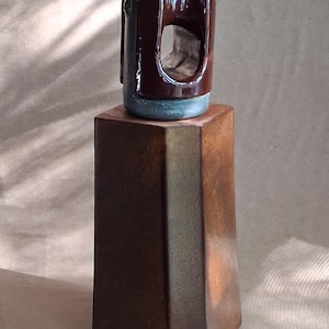 May include: A dark brown, decorative object with a rounded top and a rectangular base. The top portion has a curved design with a central opening. The base is a dark brown, geometric shape. The object is likely a sculpture or decorative item.