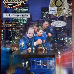 May include: A blue die-cast Paddy Wagon toy car from the Road Champs series. The packaging features a police badge and a photo of police officers. The toy has real rubber tires and authentic police car detail.
