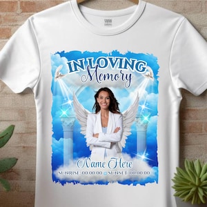 Puede incluir: Camiseta blanca con un dise&ntilde;o gr&aacute;fico azul y blanco que presenta a una mujer con alas de &aacute;ngel. El gr&aacute;fico dice "In Loving Memory" y tiene espacio para un nombre, la salida y la puesta del sol.