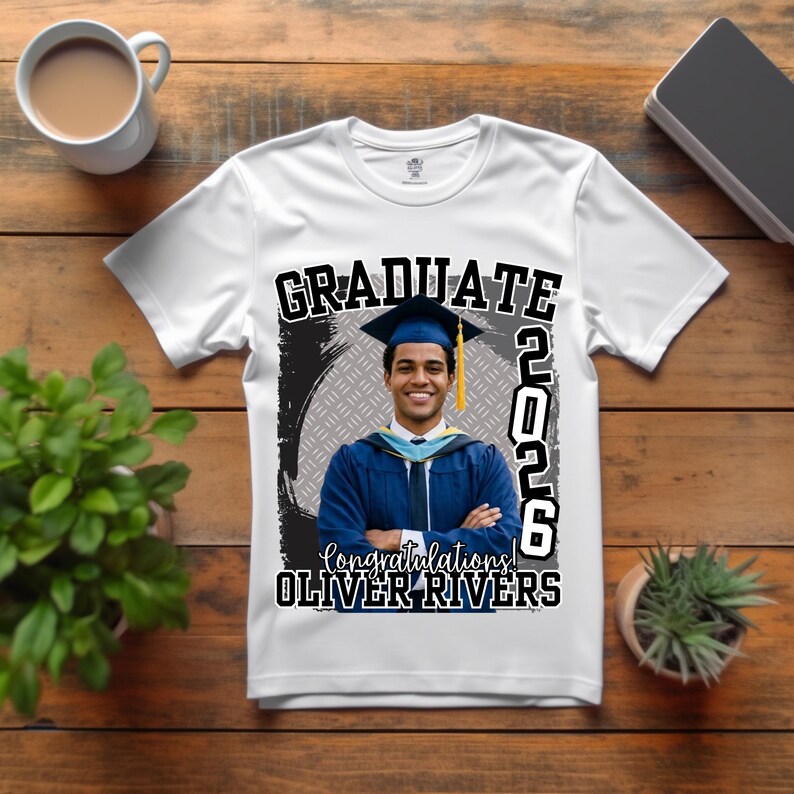 May include: White t-shirt featuring a graduation design. The design includes the word "GRADUATE" in bold black letters, the year "2026", and the name "OLIVER RIVERS". A photo of a graduate in a cap and gown is also featured.