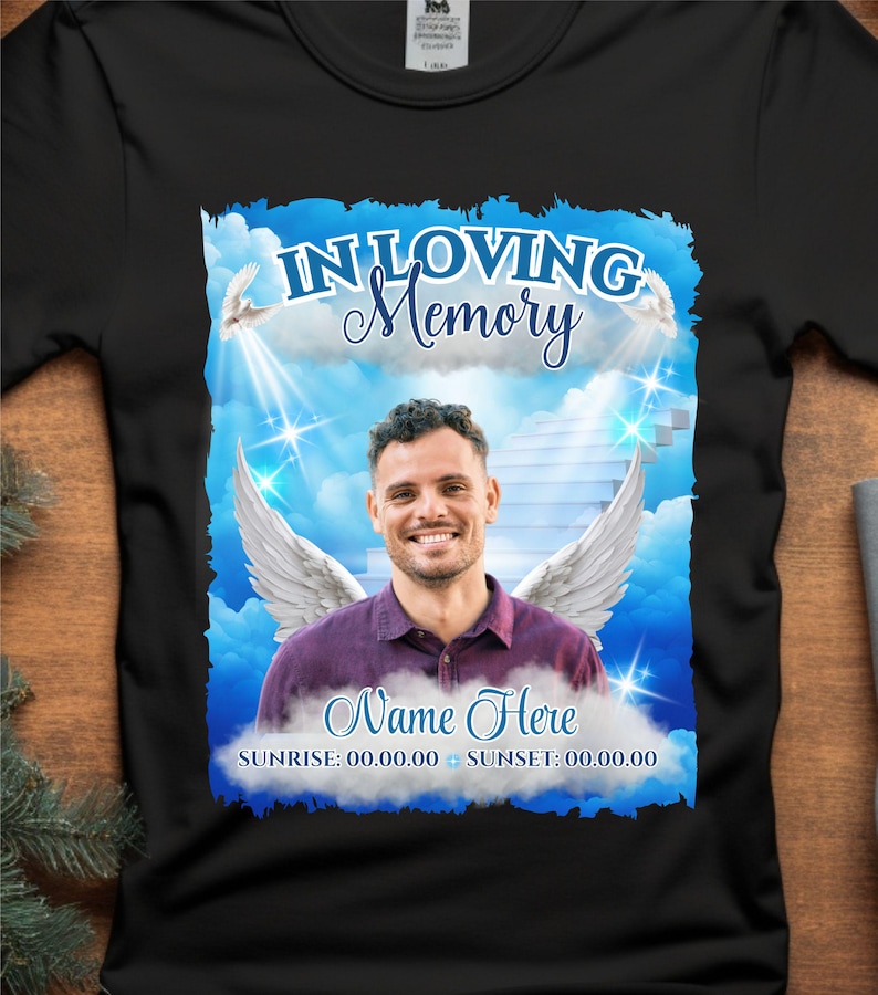 Puede incluir: Una camiseta negra con un gr&aacute;fico azul y blanco de un hombre con alas de &aacute;ngel frente a un cielo nublado. El gr&aacute;fico incluye el texto "In Loving Memory", "Name Here", "Sunrise: 00.00.00", y "Sunset: 00.00.00".