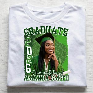 May include: White t-shirt featuring a graduation design. The design includes the word "GRADUATE" in green, the year "2026", and the words "Congratulations!" and "AMANDA SMITH". A woman in a graduation cap and gown is in the center.