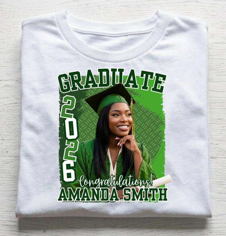 May include: White t-shirt featuring a graduation design. The design includes the word "GRADUATE" in green, the year "2026", and the words "Congratulations!" and "AMANDA SMITH". A woman in a graduation cap and gown is in the center.