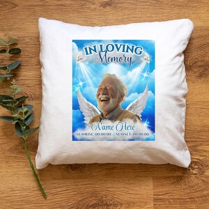 Puede incluir: Almohada blanca con un dise&ntilde;o impreso en azul y blanco. El dise&ntilde;o presenta a un hombre con alas, nubes y estrellas. El texto dice "In Loving Memory", "Name Here", "Sunrise: 00.00.00 Sunset: 00.00.00".