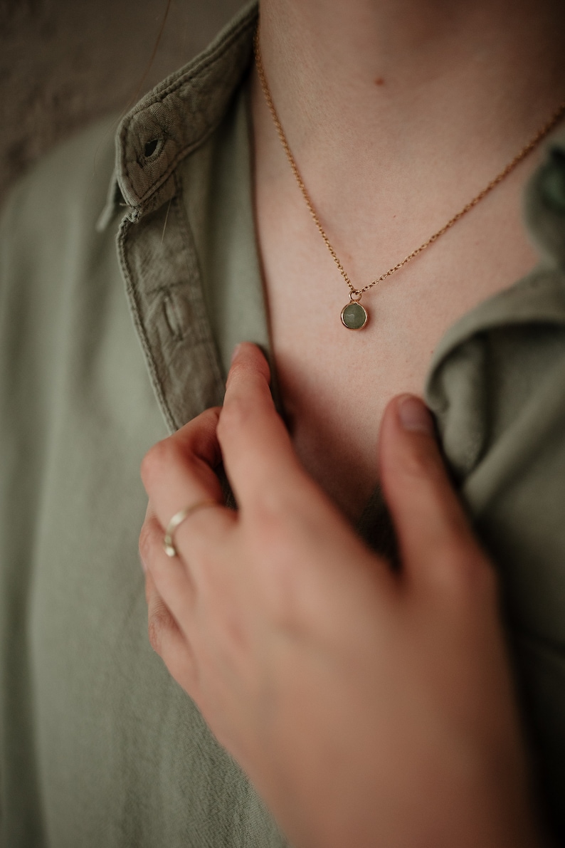 Puede incluir: Un collar de cadena de oro con un peque&ntilde;o colgante redondo de piedra preciosa verde.