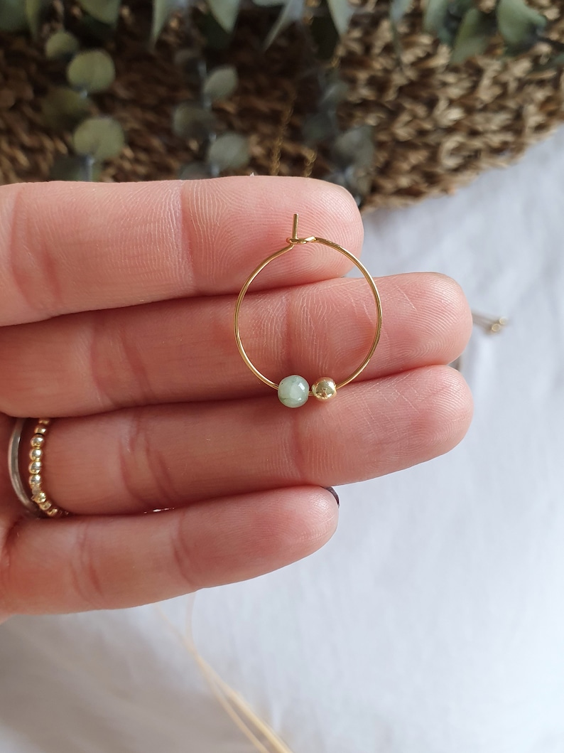 Puede incluir: Un aro de oro para la oreja con una peque&ntilde;a piedra verde y una perla dorada.