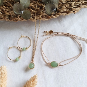 Puede incluir: Un conjunto de joyas de piedra verde que incluye un collar, pendientes y una pulsera. El collar y los pendientes tienen detalles dorados, mientras que la pulsera est&aacute; hecha de un cord&oacute;n beige.