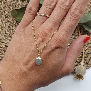 Puede incluir: Un collar de cadena dorada con un colgante de piedra preciosa verde claro. El collar se lleva en la mu&ntilde;eca de una persona.