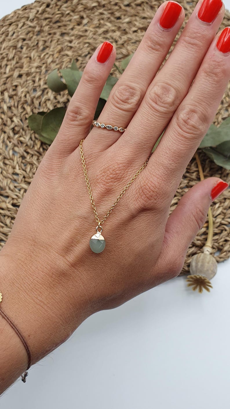 Puede incluir: Un collar de cadena dorada con un colgante de piedra preciosa verde claro. El collar se lleva en la mu&ntilde;eca de una persona.