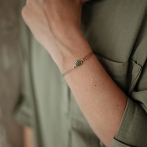 Puede incluir: Un brazalete delicado con un dije de piedra preciosa verde en una cadena dorada.