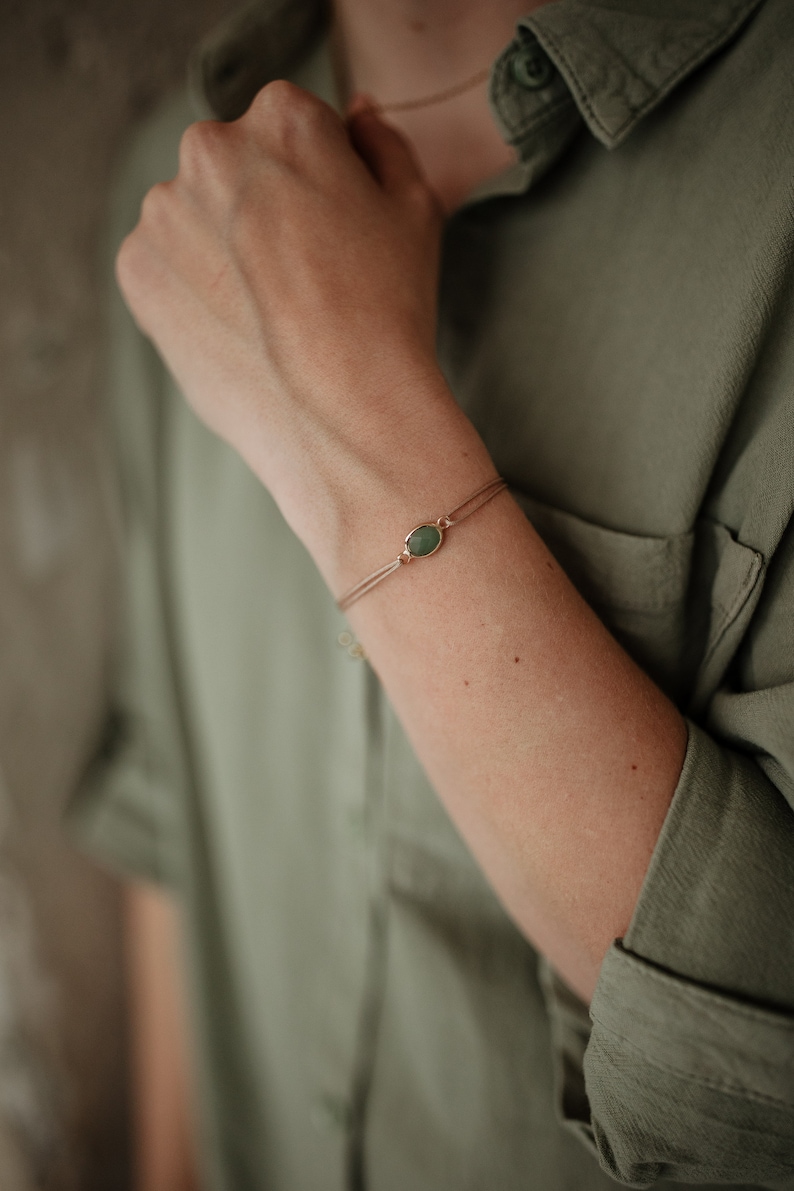 Puede incluir: Un brazalete delicado con un dije de piedra preciosa verde en una cadena dorada.