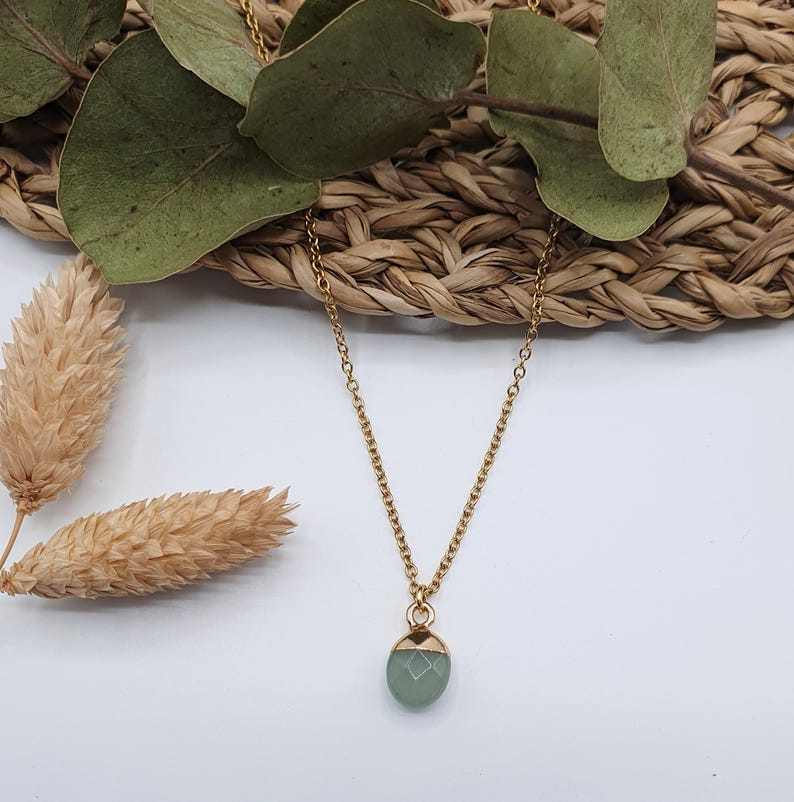 Puede incluir: Un collar de cadena dorada con un colgante de piedra preciosa verde claro.