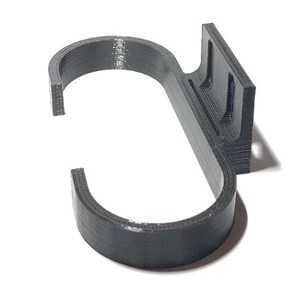 May include: A dark gray, 3D-printed hook with a curved design. The hook features a rectangular mounting plate with two slots for attachment. The hook is designed to hang items and is made of a durable material.