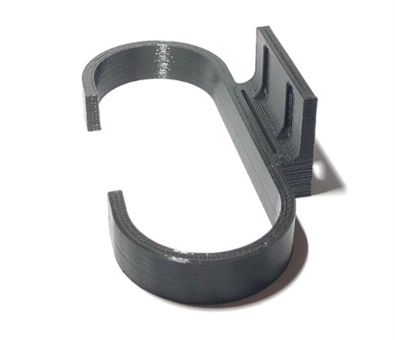 May include: A dark gray, 3D-printed hook with a curved design. The hook features a rectangular mounting plate with two slots for attachment. The hook is designed to hang items and is made of a durable material.