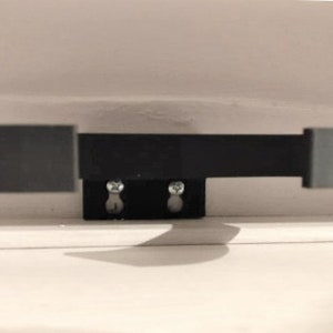 May include: A black metal cabinet door pull with two circular ends and a rectangular connecting bar. The pull is mounted on a black rectangular base with two screws. The hardware is designed for a cabinet or drawer.