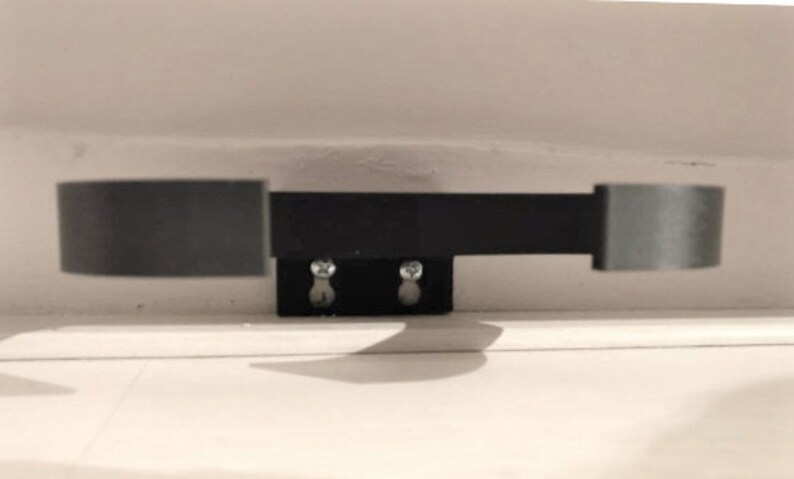 May include: A black metal cabinet door pull with two circular ends and a rectangular connecting bar. The pull is mounted on a black rectangular base with two screws. The hardware is designed for a cabinet or drawer.