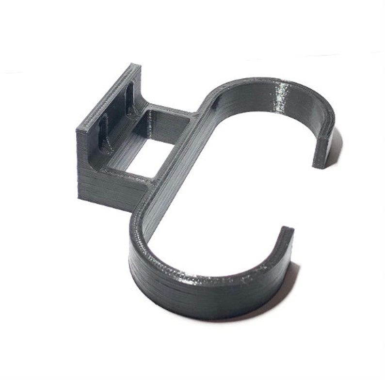 May include: A dark gray, 3D-printed wall-mounted hook. The hook features a rectangular mounting plate with two holes, a square opening, and a curved hook shape. The object is designed to hold items and is made of plastic.