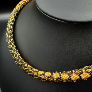Peut inclure: Un collier de perles noires et dorées avec un motif géométrique. Le collier est présenté sur un buste de mannequin noir.