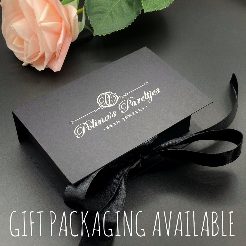 May include: A black gift box with a white ribbon and the text "Polina's Parelyjes - Bead Jewelry" printed on the top. The box is sitting on a gray surface.  GIFT PACKAGING AVAILABLE is printed in white on a black background.
