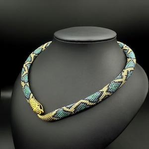May include: A beaded snake necklace with a gold snake head clasp. The necklace is made with black, green, and gold beads.