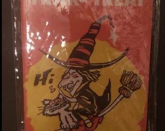 Könnte beinhalten: Eine rote und gelbe Halloween-Karte mit einer Hexe und einer Katze, die auf einem Besen fliegen. Die Karte trägt oben den Schriftzug "Trick or Treat" und neben der Hexe steht "Hi!"
