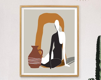 May include: A framed abstract art print with a beige background, a brown and orange arch, a black and white figure, and a brown and white vase. The print is hanging on a white wall with a gold metal sunburst mirror above it. A potted cactus plant is in the foreground.