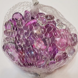 May include: A bag of iridescent purple and clear glass gems. The gems are in a mesh bag and are perfect for crafts or home decor.