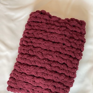 May include: A burgundy knitted throw pillow with a chunky knit texture.