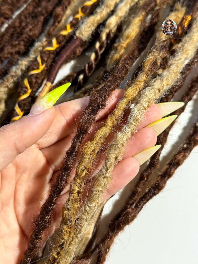 May include: Close-up of brown, blonde, and dark brown dreadlocks. The dreadlocks are a mix of colors and textures, with some having a twisted appearance. Some dreadlocks have yellow accents. The image is well-lit, showcasing the details of the hair.