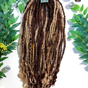 May include: A set of brown and blonde dreadlocks with wavy ends. The dreadlocks are a mix of dark brown, light brown, and blonde colors. A small tag with a logo is attached to the dreadlocks.