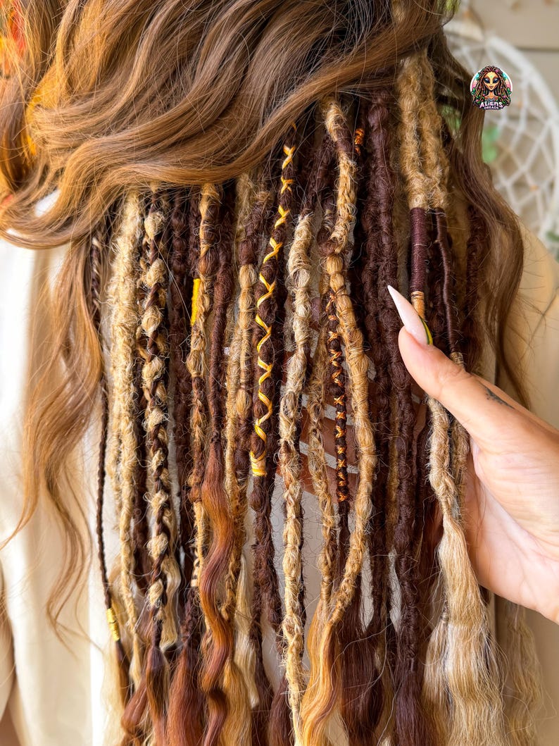 May include: A close-up of brown and blonde dreadlocks with yellow and brown accents. The dreadlocks are styled with various textures and patterns, including braids and wrapped sections. The hair is styled with a natural look.
