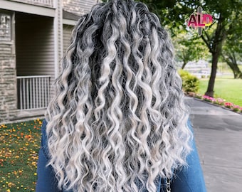 Pode incluir: Uma pessoa com cabelo comprido, encaracolado, preto e branco. O cabelo está penteado em um padrão ondulado solto. A pessoa está vestindo uma camisa azul de manga comprida.