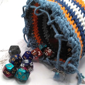 May include: A blue, white, and orange crocheted dice bag with a silver charm hanging from it. The bag is open and several multi-colored dice are spilling out.