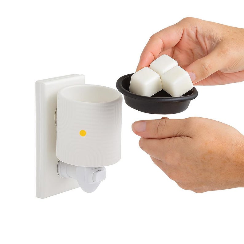 Peut inclure: Un diffuseur de cire blanc &agrave; brancher, de forme cylindrique, avec un voyant lumineux jaune. Un petit plat noir contient trois cubes de cire blancs. Le diffuseur est branch&eacute; dans une prise murale blanche.