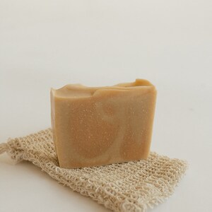 May include: A bar of natural soap with a light brown color and a marbled pattern, resting on a beige exfoliating washcloth.