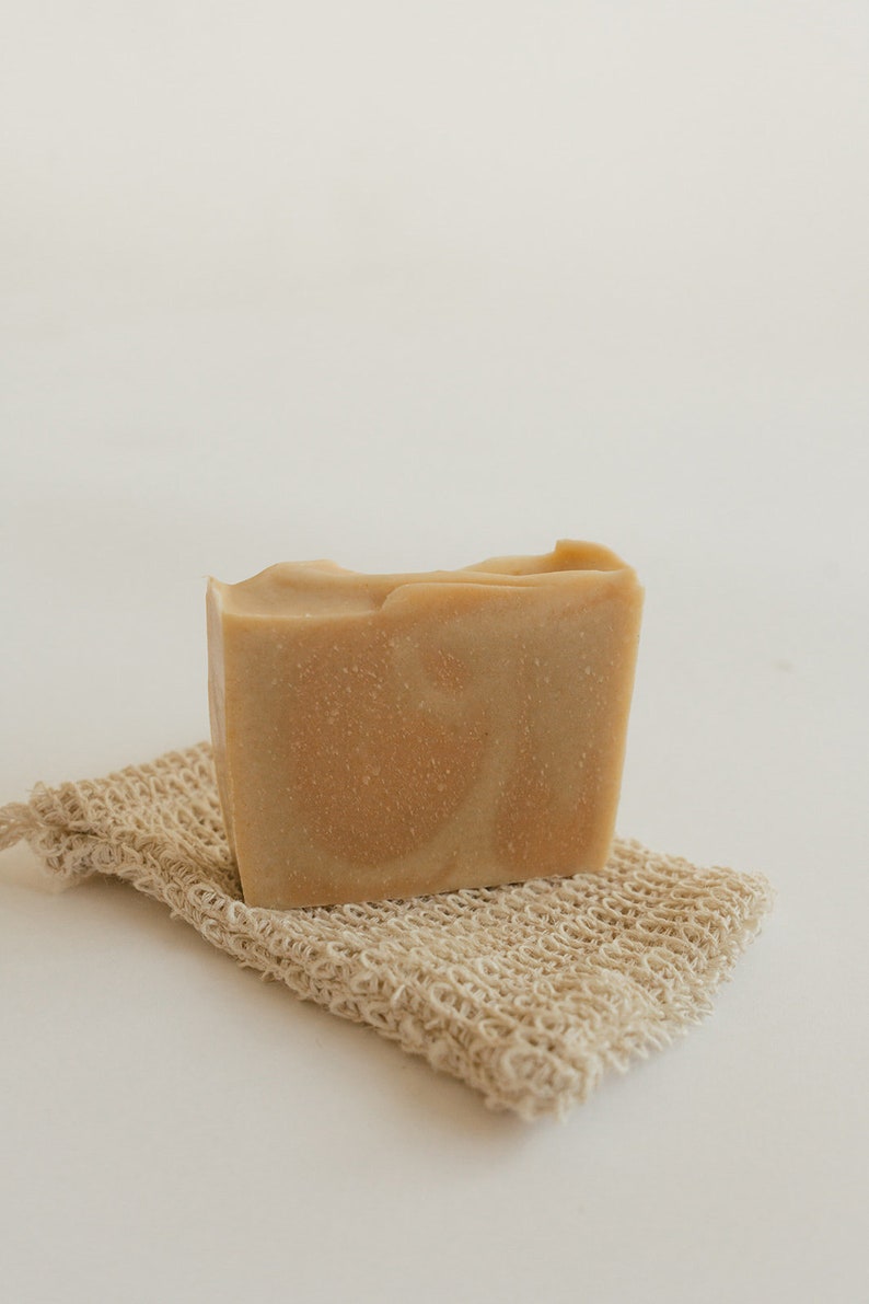 May include: A bar of natural soap with a light brown color and a marbled pattern, resting on a beige exfoliating washcloth.