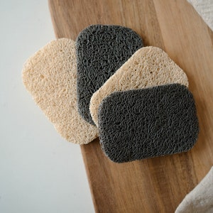 May include: Four kitchen scrubbers, two beige and two dark gray, made of a woven material, on a wooden surface.