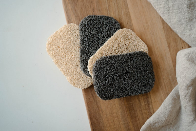 May include: Four kitchen scrubbers, two beige and two dark gray, made of a woven material, on a wooden surface.