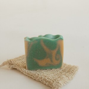 May include: A green and orange bar of soap on a natural fiber soap saver.