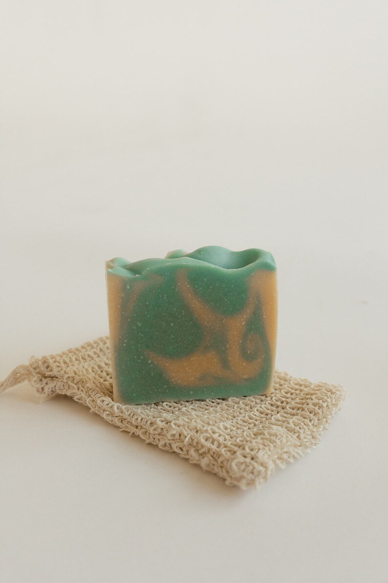 May include: A green and orange bar of soap on a natural fiber soap saver.