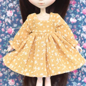 Peut inclure: Une robe jaune &agrave; motif floral blanc et manches longues. La robe a une taille fronc&eacute;e et une jupe l&eacute;g&egrave;rement &eacute;vas&eacute;e.