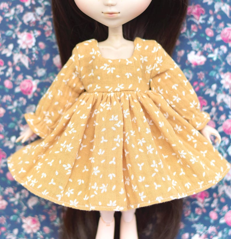 Peut inclure: Une robe jaune &agrave; motif floral blanc et manches longues. La robe a une taille fronc&eacute;e et une jupe l&eacute;g&egrave;rement &eacute;vas&eacute;e.