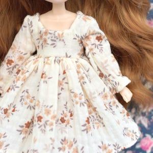 Peut inclure: Une robe blanche &agrave; motif floral dans les tons brun et beige. La robe a des manches longues et une jupe pliss&eacute;e.