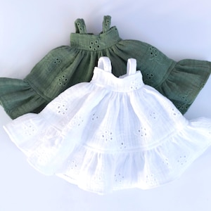 May include: Two doll dresses, one white and one green, with eyelet detailing and ruffled hems.