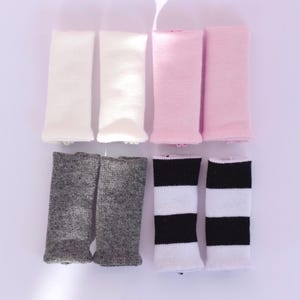 Pode incluir: Uma variedade de polainas em várias cores. A coleção inclui pares em branco, rosa claro, cinza e listras em preto e branco. Cada par é tricotado com punho canelado.