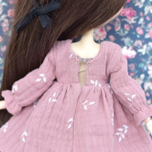 Peut inclure: Une robe rose avec des broderies de feuilles blanches et une fermeture &agrave; fermoir argent&eacute;e dans le dos.